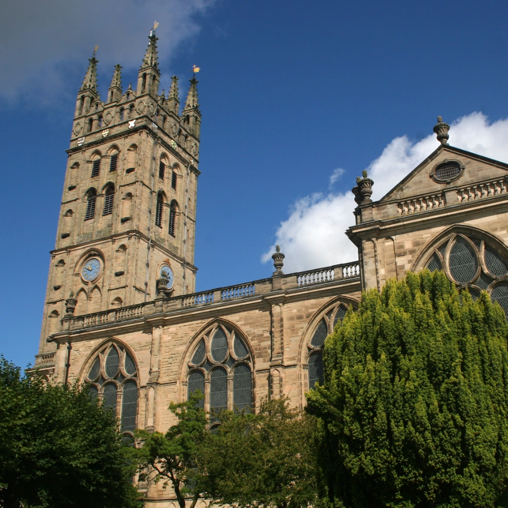 Exterior of the Collegiate Church of St Mary in Warwick, showing its tall stone Gothic tower and church façade with pointed arches, buttresses, and historic architectural details in the centre of the town.