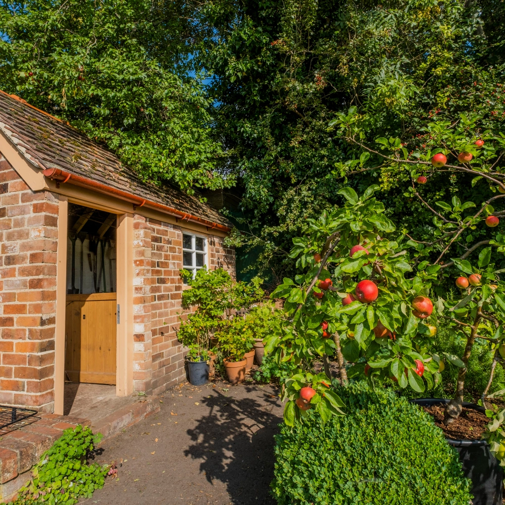 View of Hill Close Gardens in Warwick — a series of small, individual Victorian-style garden plots separated by tall green hedges, featuring colourful flowerbeds, lawns, pathways and quaint summerhouses nestled among lush planting, creating a tranquil historic garden setting.